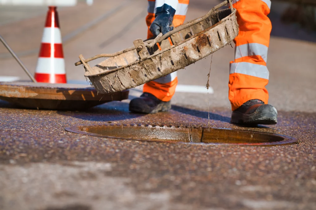 Hofele Mitarbeiter hebt eine verschmutzte Abdeckung bei Arbeiten an einem Kanalschacht an