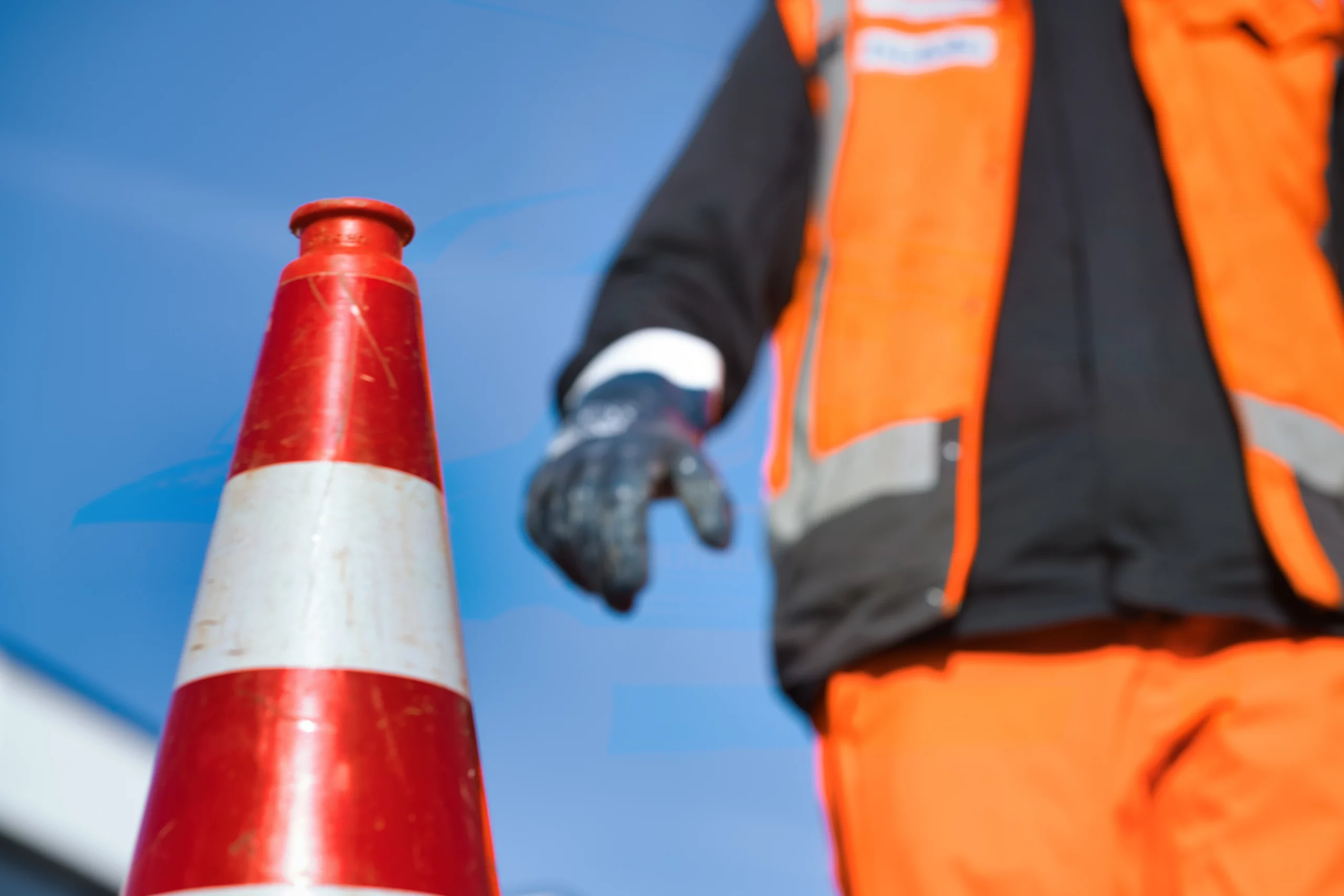 Verkehrsleitkegel mit Mitarbeiter in orangefarbener Arbeitskleidung im Hintergrund
